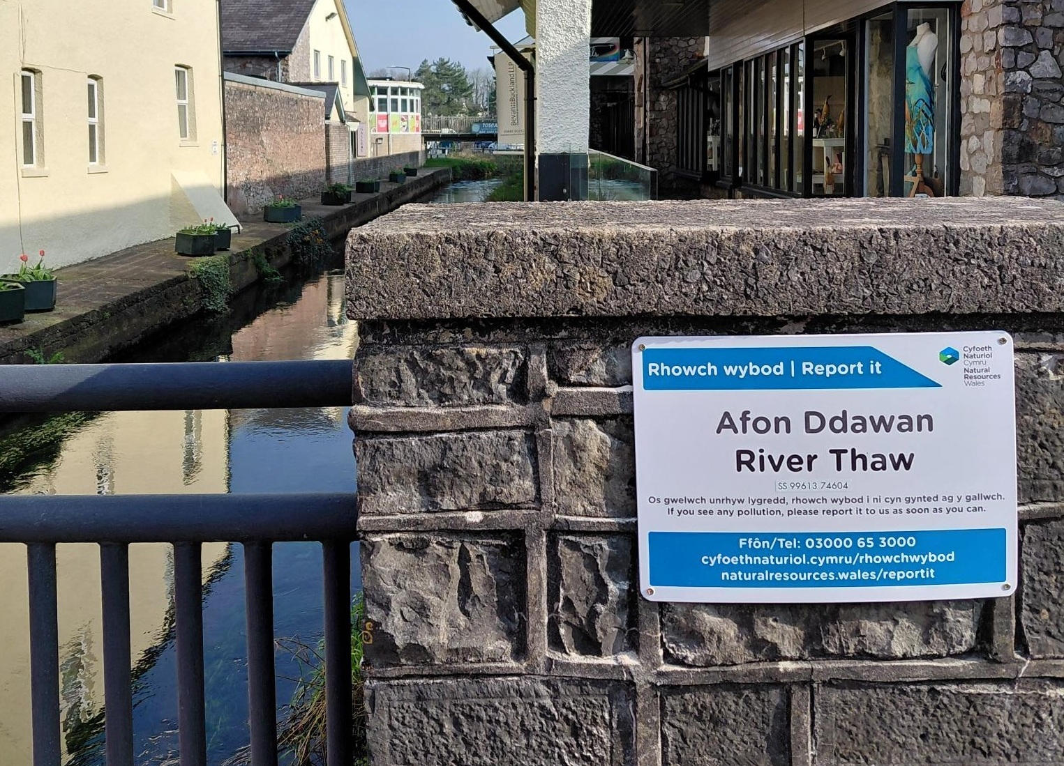 A sign placed on a wall next to a river 