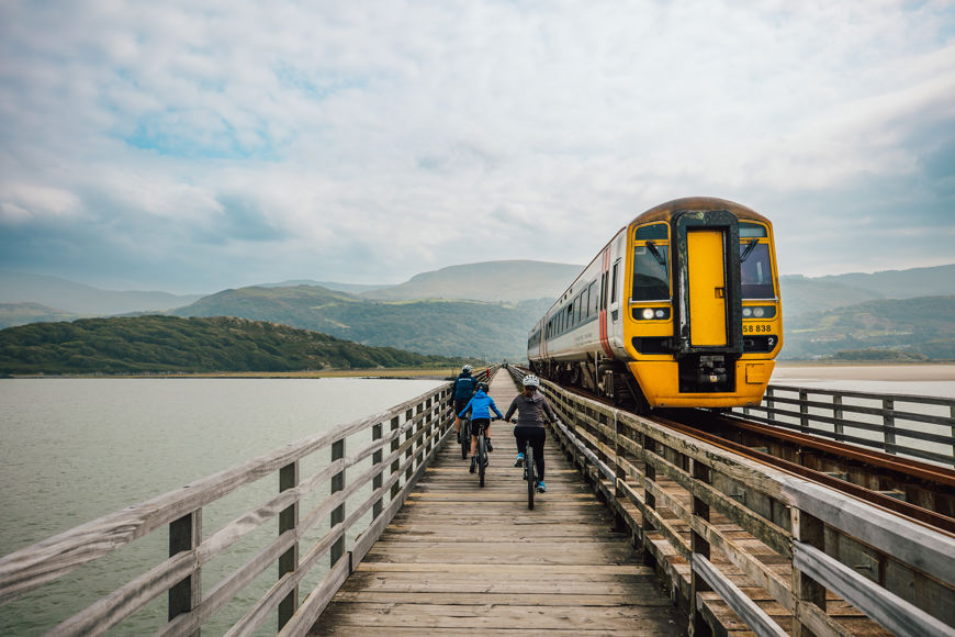 Beicwyr yn beicio wrth ymyl trên