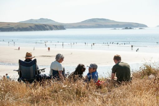 Teulu Yn Y Twyni Yn Whitesand, Sir Benfro, Gyda Thraeth Prysur y tu ôl iddyn nhw.