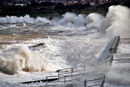 Coastal storm surge at Colwyn Bay with coastal defences visible.
