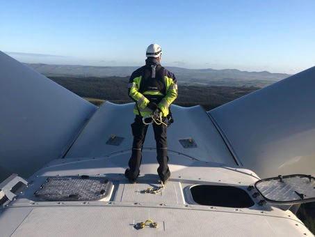 Turbine engineer standing on top of wind turbine looking out at Welsh landscape