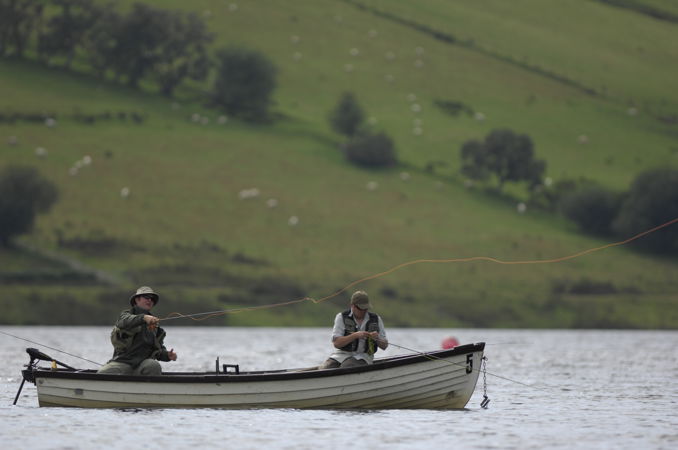 Two men sat in a boat on a river fishing Two men sat in a boat on a river fishing