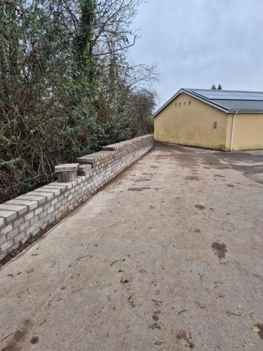 Photo of a new brick wall alongside a concrete parking area