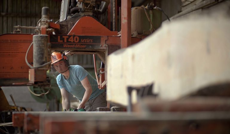 Man working in a saw mill cutting large piece of timber Man working in a saw mill cutting large piece of timber