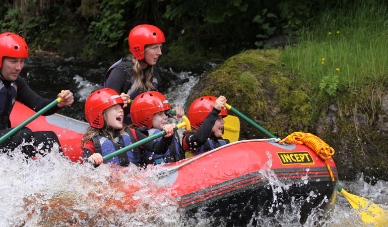 Children and adults paddling in a boat down rapids Children and adults paddling in a boat down rapids