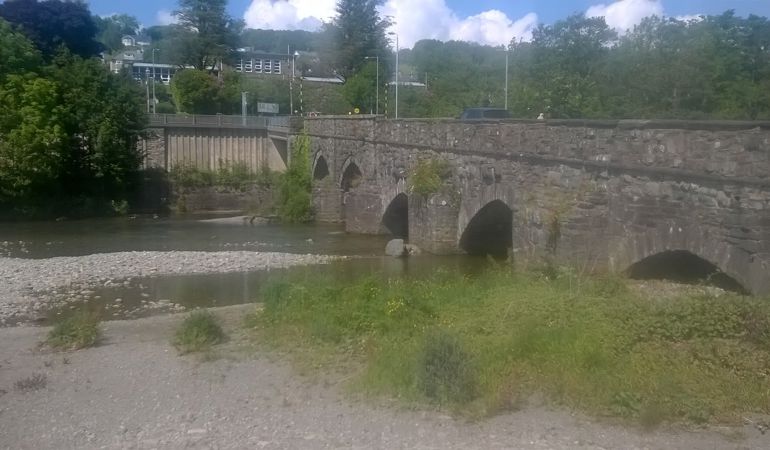 Low level river flowing under a bridge with multiple arches Low level river flowing under a bridge with multiple arches