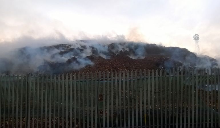 Smoke bellowing from a pile of wood chip surrounded by a metal fence Smoke bellowing from a pile of wood chip surrounded by a metal fence
