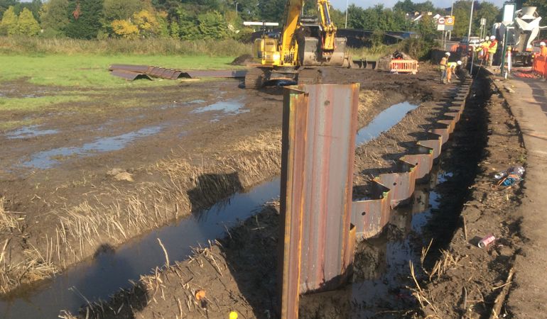 Digger in a muddy field building a steal flood defence Digger in a muddy field building a steal flood defence