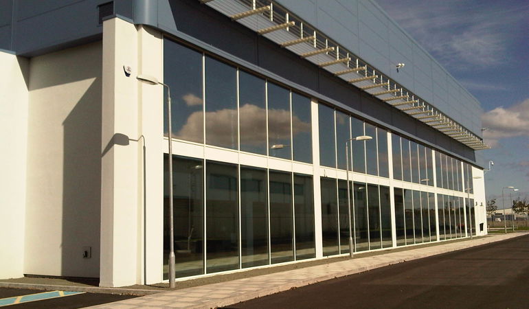 Long building with floor to ceiling glass windows and a grey roof Long building with floor to ceiling glass windows and a grey roof