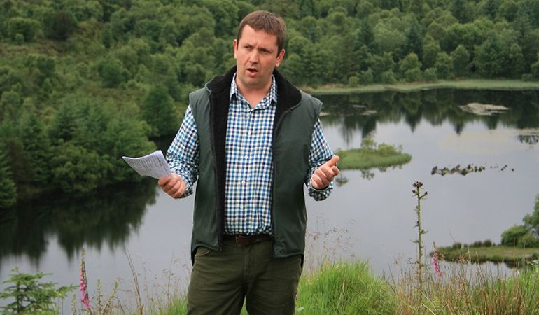 Man in checked shirt and waistcoat stood at the side of a lake with piece of paper in his hand Man in checked shirt and waistcoat stood at the side of a lake with piece of paper in his hand