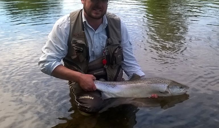 Angler holding a salmon while standing in the River Usk Angler holding a salmon while standing in the River Usk