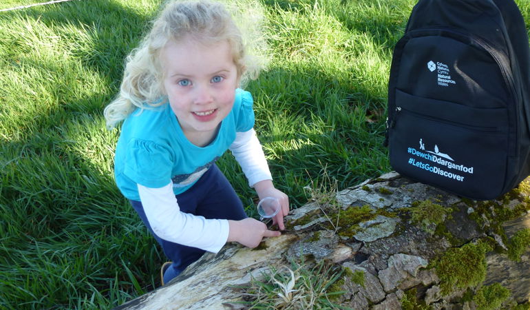 Little girl using a bug pot to collect insects next to a discovery backpack Little girl using a bug pot to collect insects next to a discovery backpack