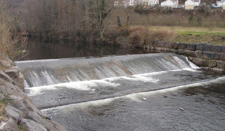 Llun o gored Ynysowen yn edrych i fyny'r afon Taf gyda dŵr yn rhaeadru i lawr yr afon dros y gored Llun o gored Ynysowen yn edrych i fyny'r afon Taf gyda dŵr yn rhaeadru i lawr yr afon dros y gored