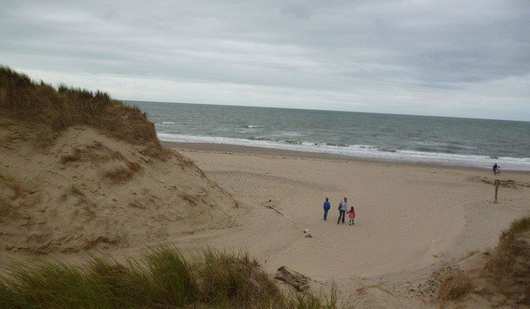 People on a beach near some sand dunes People on a beach near some sand dunes