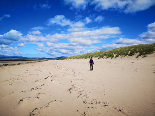 Woman walking on the beach next to dunes