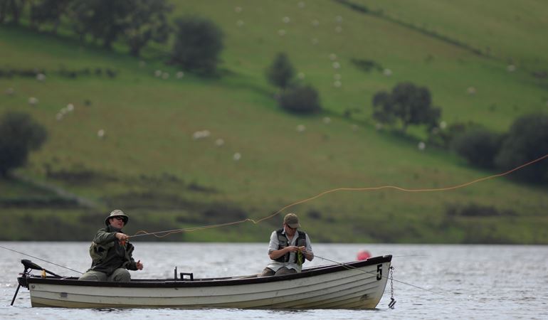 Two men sat in a boat on a river fishing 