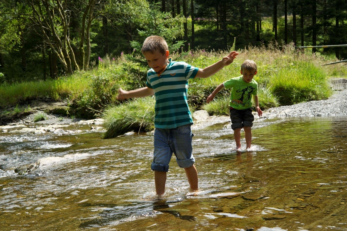 Two boys cross a shallow river barefoot.