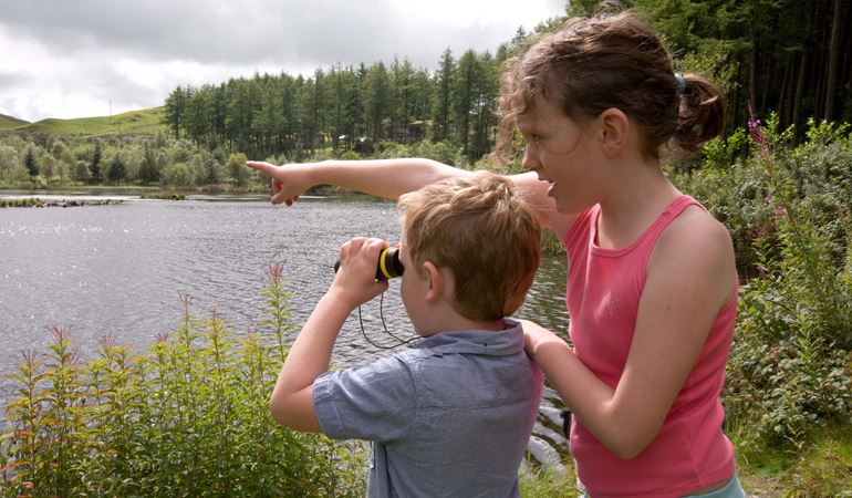 Children using binoculars at the side of a lake