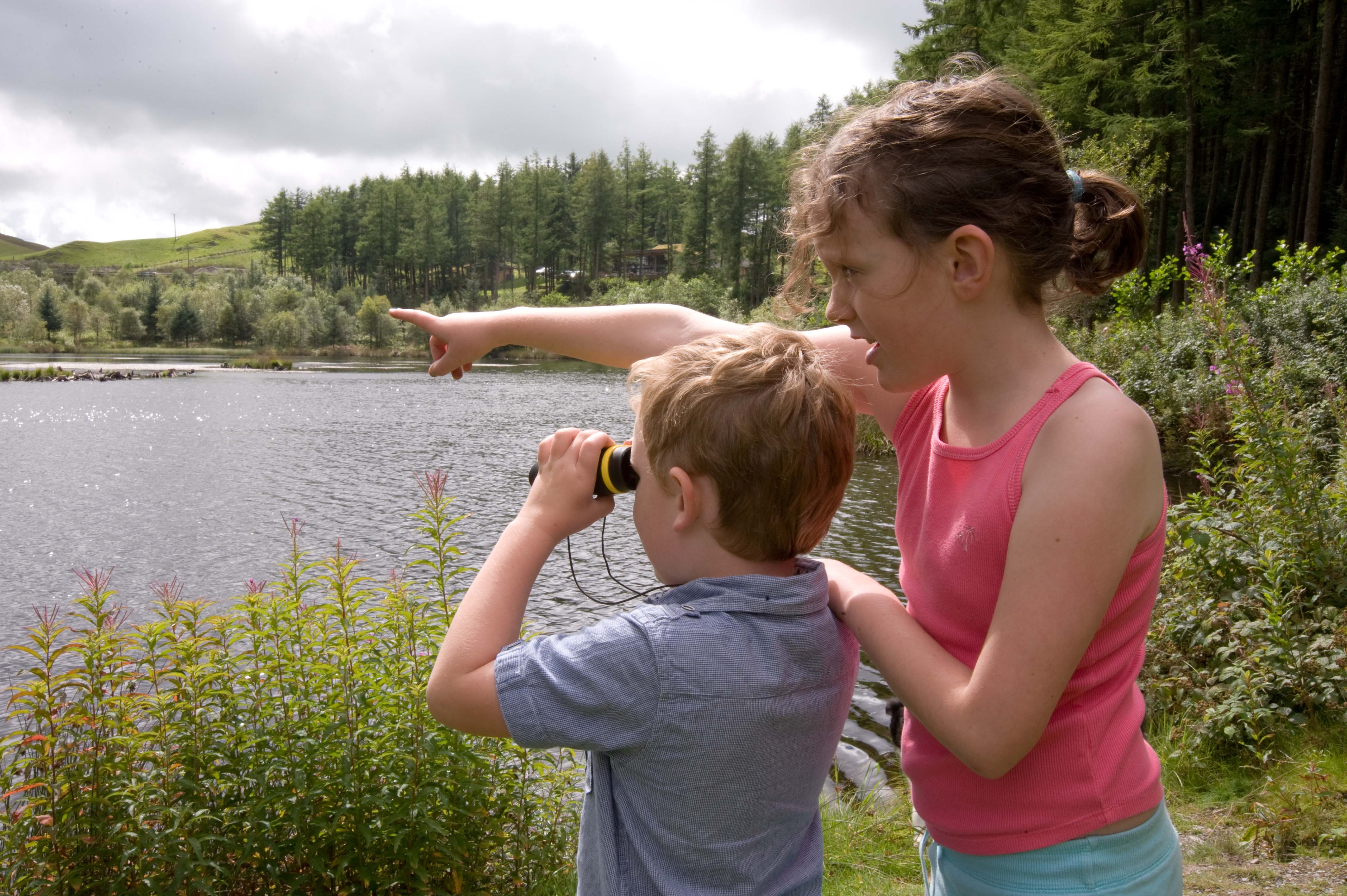 Plant yn defnyddio binocwlars ger llyn