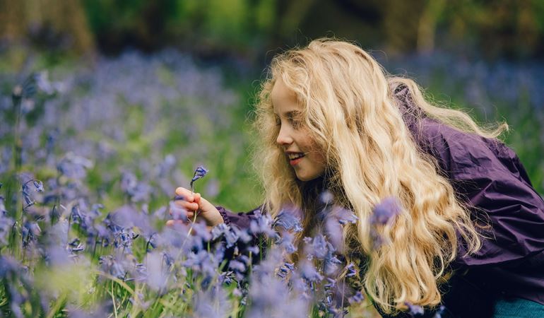 Girl looking at a bluebell in the woods 
