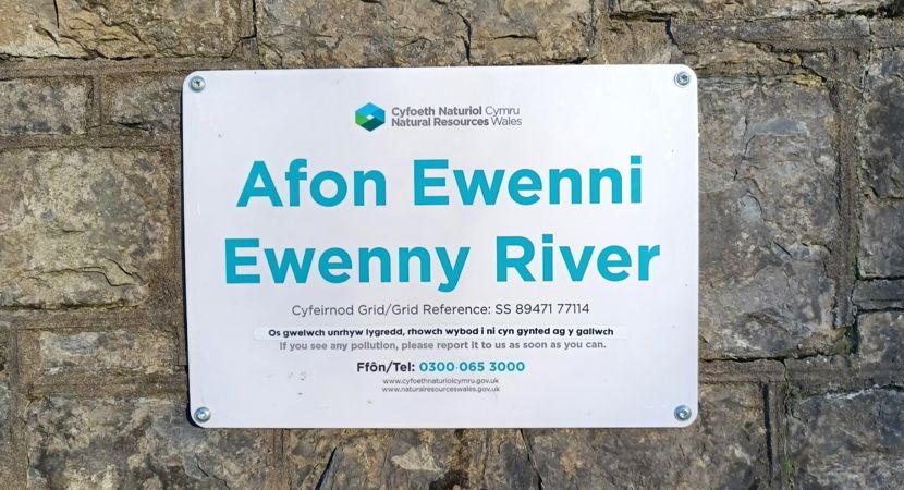 A sign on a wall next to a river with information on how to report suspected river pollution A sign on a wall next to a river with information on how to report suspected river pollution